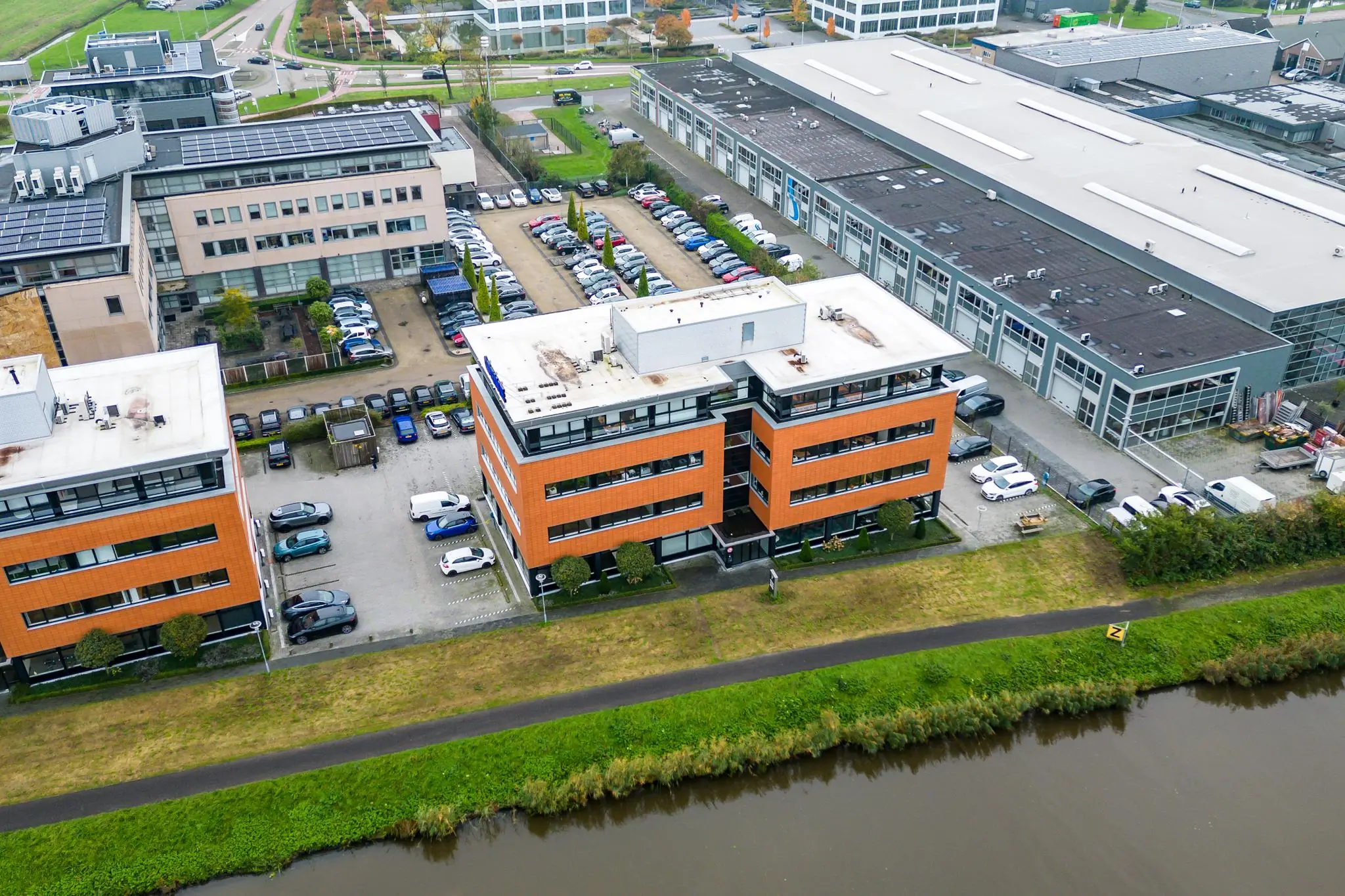Luchtfoto van kantoren en bedrijfspanden aan de Lage Biezenweg met parkeerplaatsen en een watergang op de voorgrond.